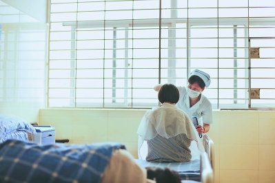 李雪梅护士长正在为一名患者理发。为了帮助患者,她自学了理发,还自己掏钱买了全套理发工具和吹风机。