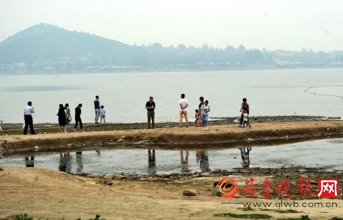 雨季未到干旱持续,游客在萌山水库库底遛狗捞