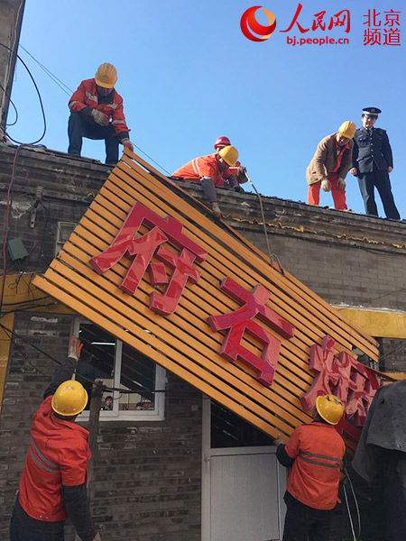 3月27日上午,北京太仆寺街12号等2处违建清理工作启动,工人们正在房顶对违建牌匾进行拆除。人民网 鲍聪颖摄