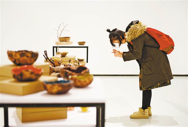 11月25日，四川美术学院虎溪校区罗中立美术馆，设计介入精准扶贫案例展现场。游客正在《传统工艺新生》展台拍摄艺术品。