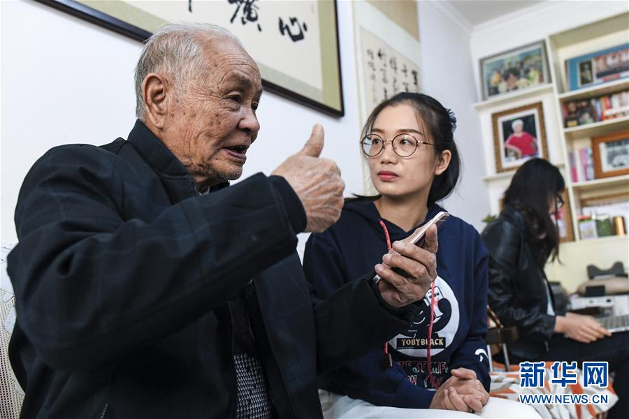 90岁的第一代老军垦陆振欧(左)在家中为石河子日报社年轻记者讲述“石河子老故事”(4月10日摄)。新华社记者王菲摄